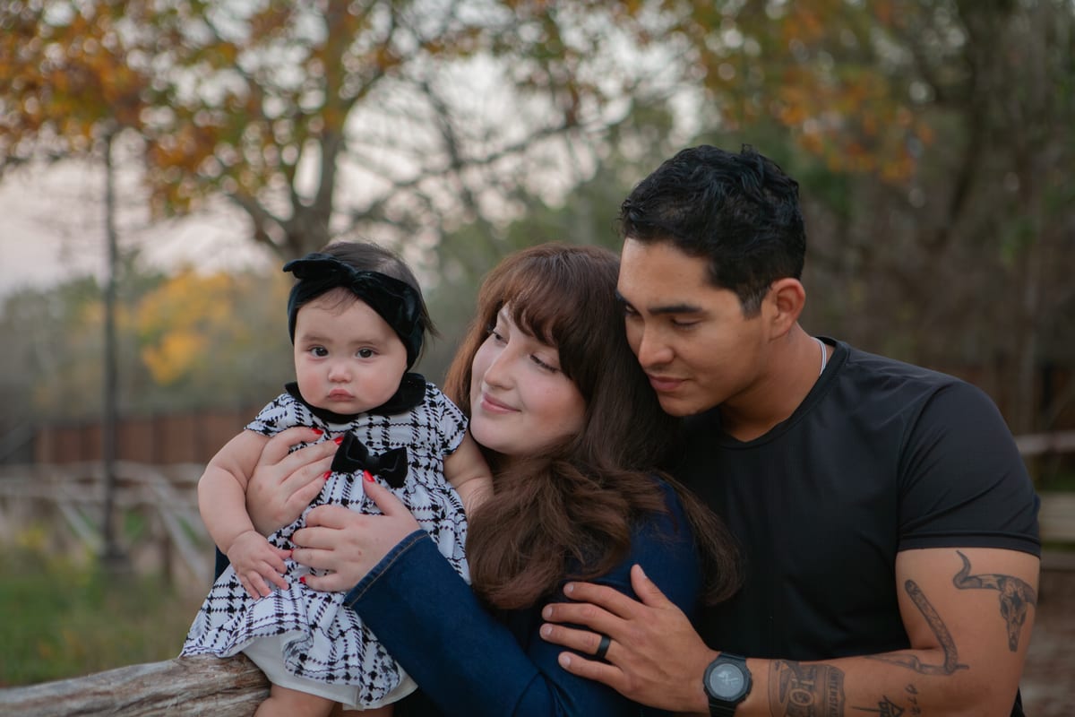 A family of three sitting together among autumn trees