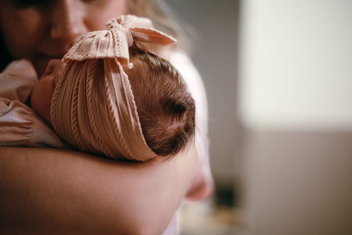 A newborn in a bow, resting on a parent’s arm