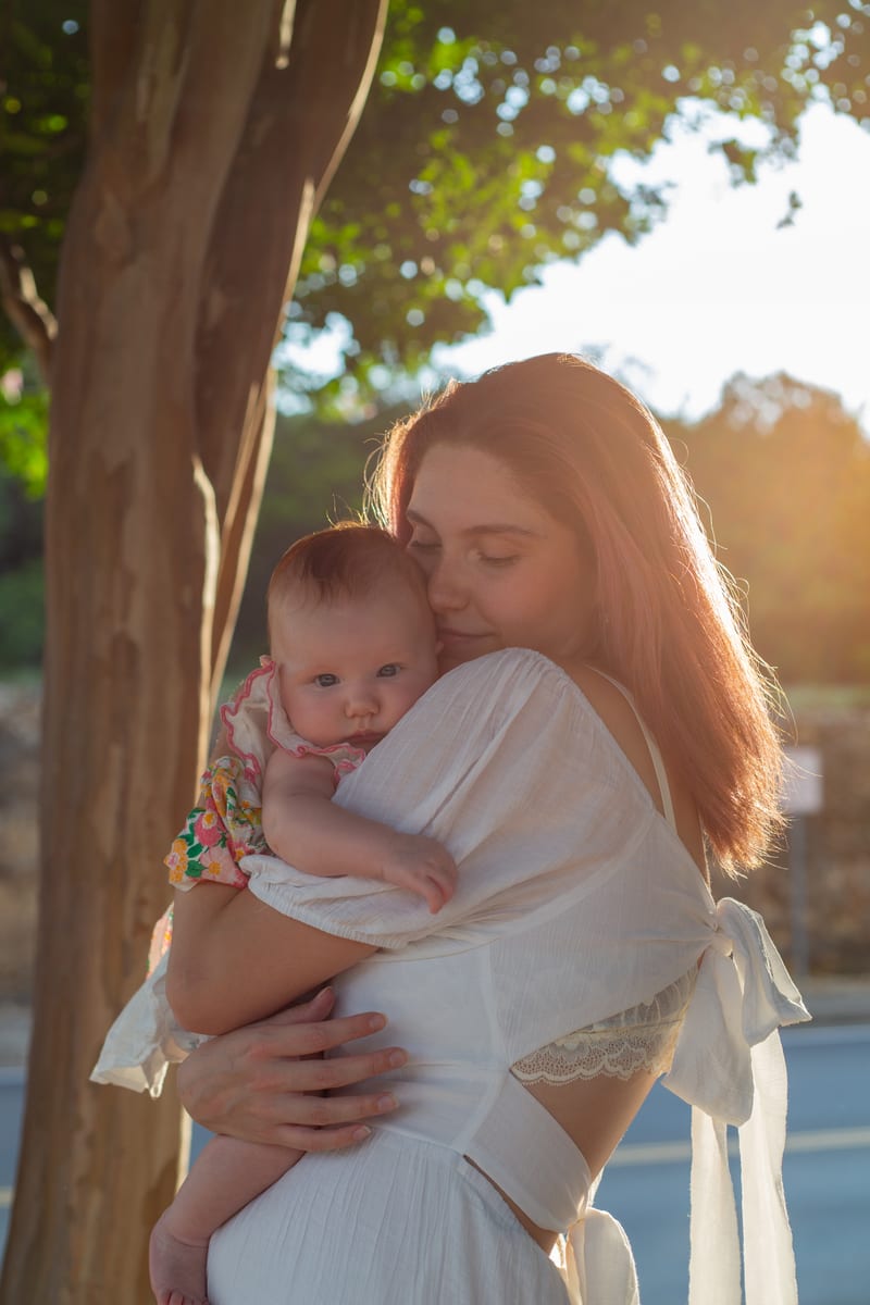 A mother holding her baby under a tree at golden hour