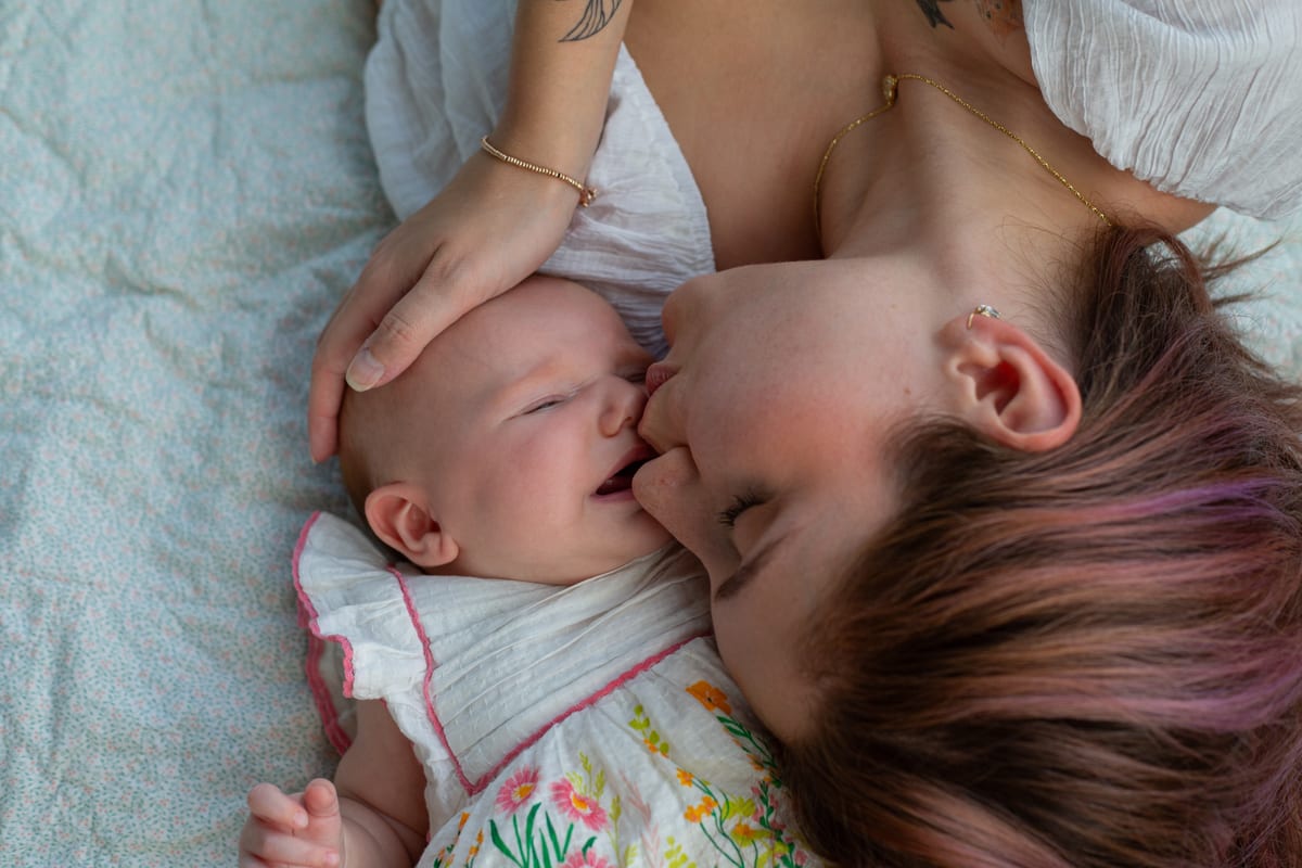 A mother kissing her baby, lying on a blanket