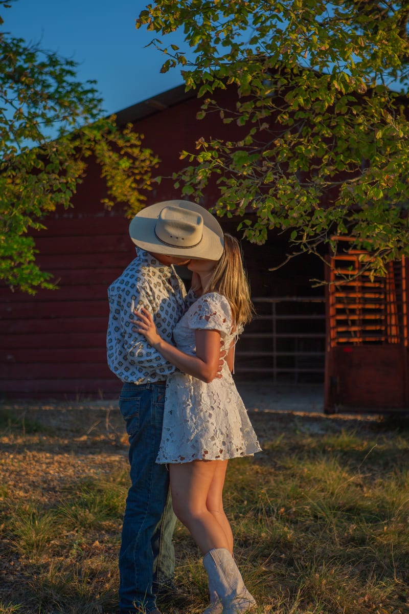 A couple kissing beside a red barn
