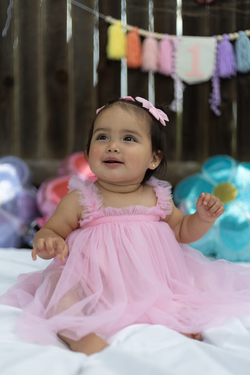 A baby in a pink tutu sitting among balloons
