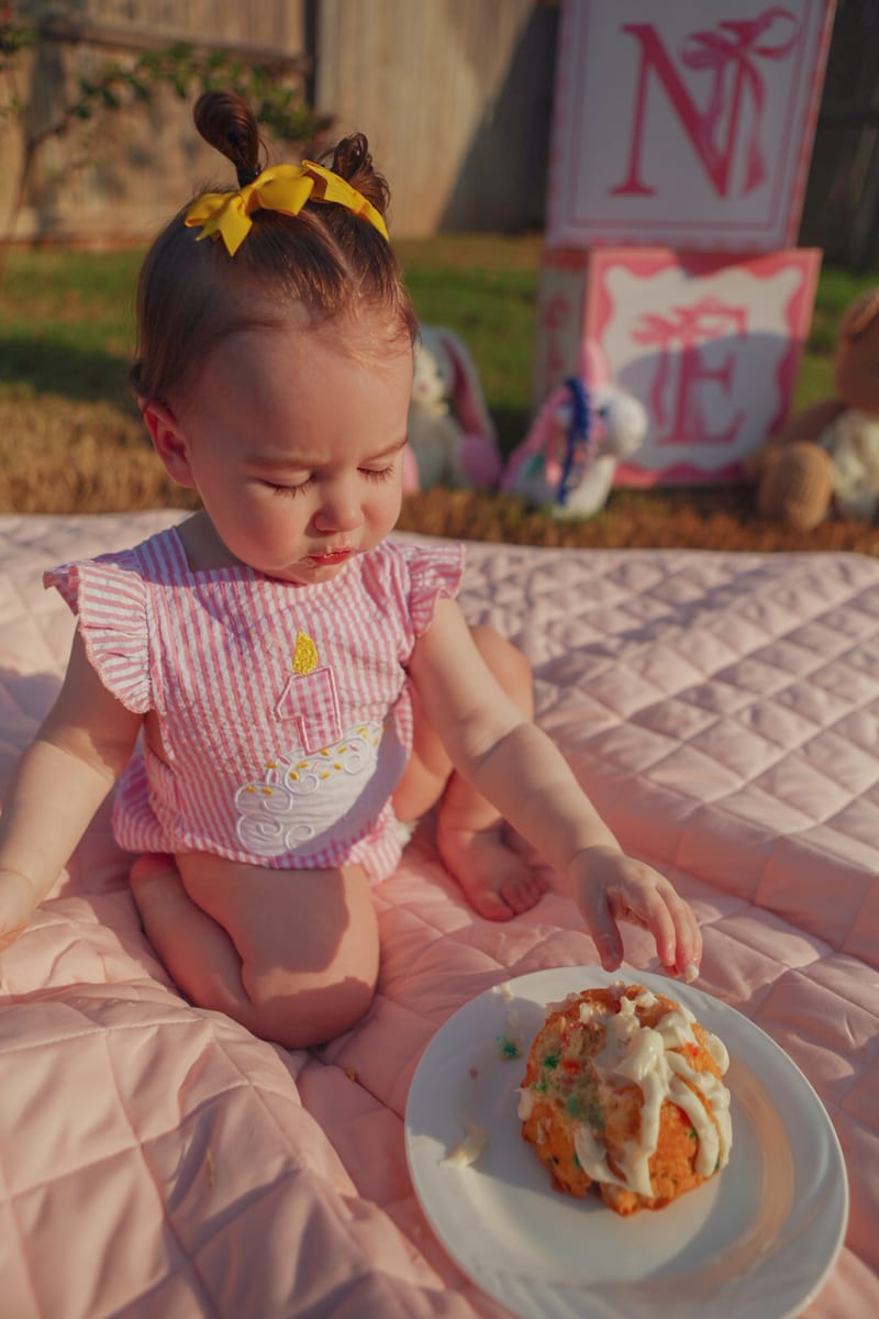 A baby reaching for a bundt cake on a pink quilt