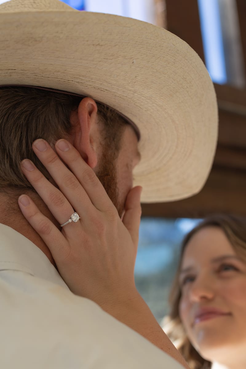 A man in a cowboy hat, her ring hand on his cheek