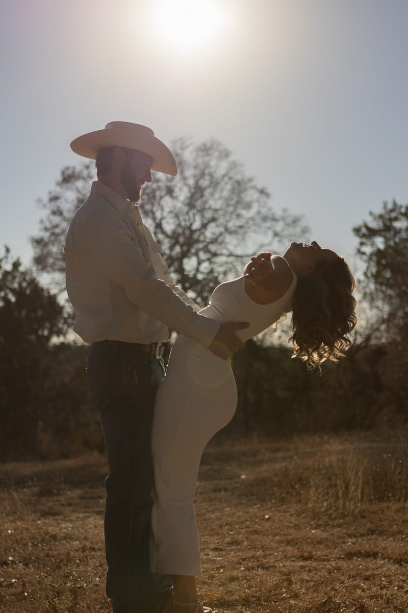 A couple at golden hour, he in a cowboy hat, she leaning back laughing