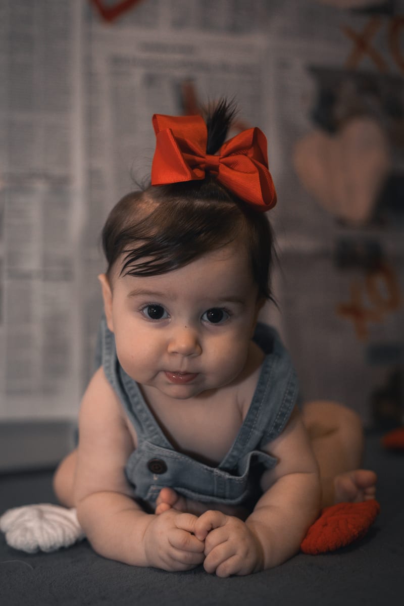 A baby in denim overalls and a red bow