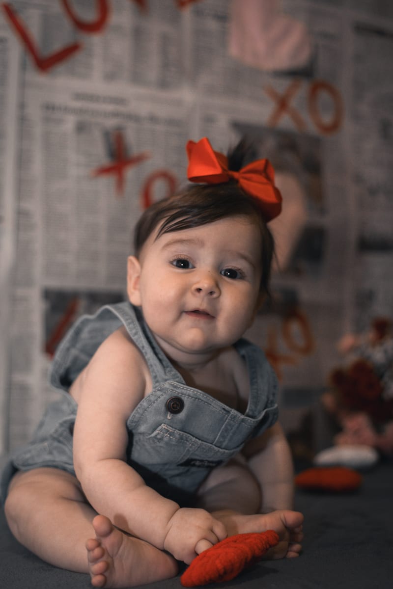 A baby in denim overalls and a red bow, smiling