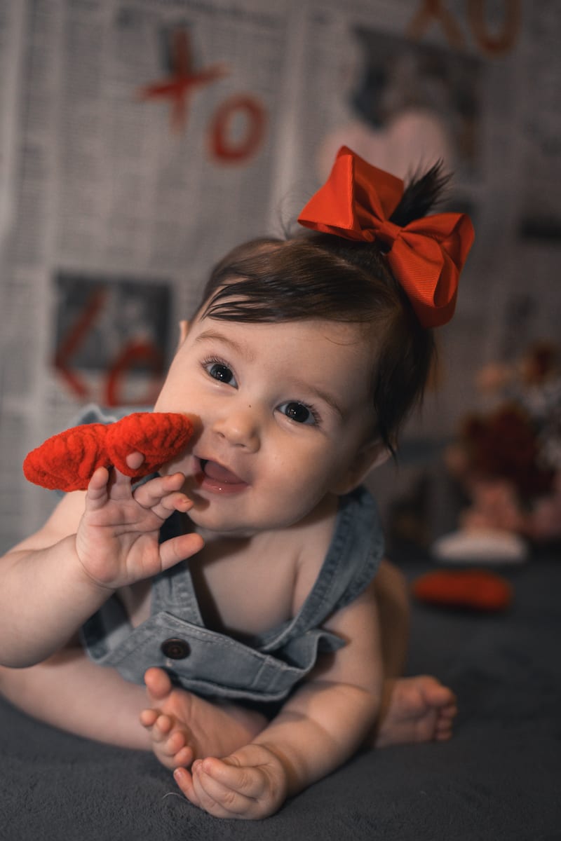 A baby in a red bow chewing on a toy
