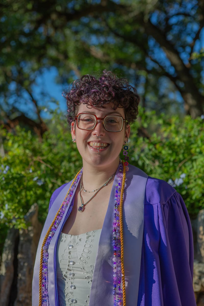 A smiling graduate in a purple gown and beaded stole, from a graduation portrait session